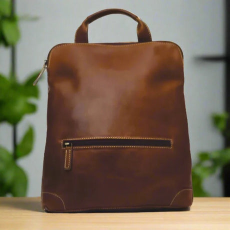 Brown leather backpack on a wooden surface with a blurred green plant background - okotoks hc pharmacy