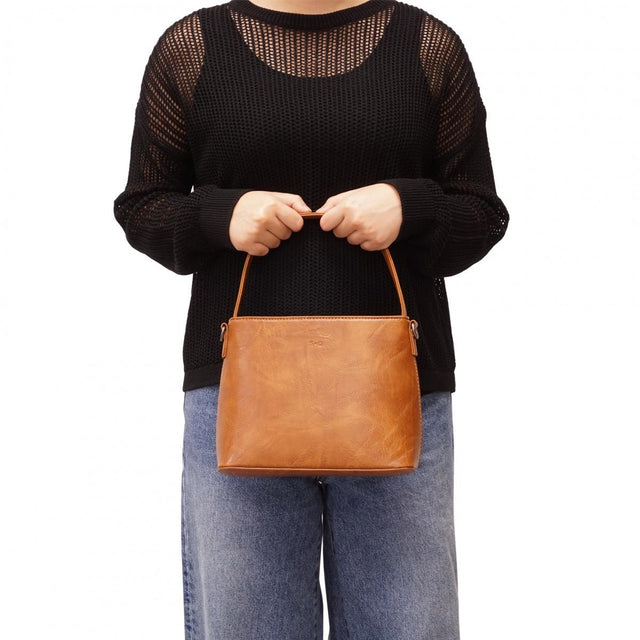 Person holding a brown leather handbag against a white background - okotoks hc pharmacy