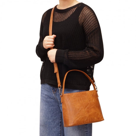 Person holding a brown leather handbag against a white background - okotoks hc pharmacy