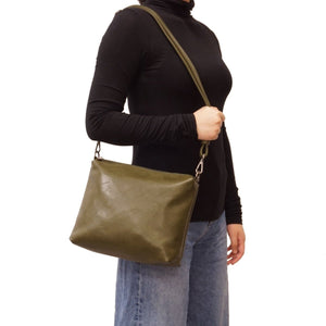 Person wearing a black turtleneck and blue jeans with an olive green shoulder bag on a white background - okotoks hc pharmacy