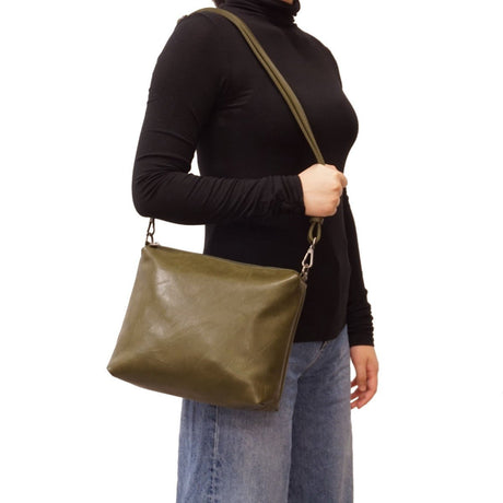 Person wearing a black turtleneck and blue jeans with an olive green shoulder bag on a white background - okotoks hc pharmacy