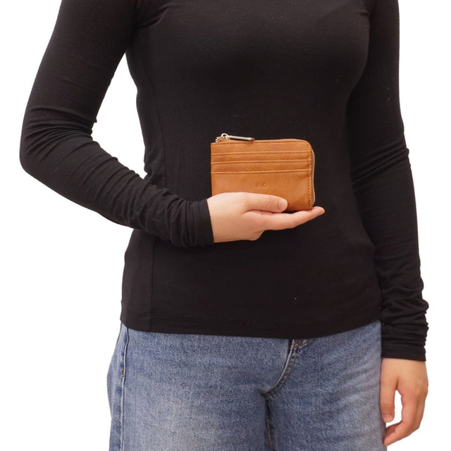 Person holding a brown leather wallet against a black long-sleeve shirt and light blue jeans on a white background - okotoks hc pharmacy