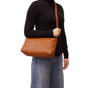 Person wearing a black turtleneck and blue jeans holding a brown leather bag on a white background - okotoks hc pharmacy