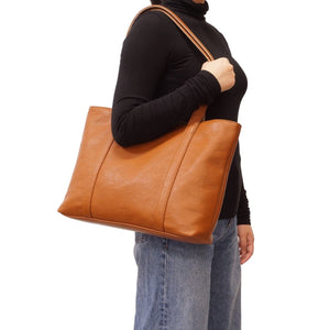 Person holding a brown leather tote bag on a white background - okotoks hc pharmacy