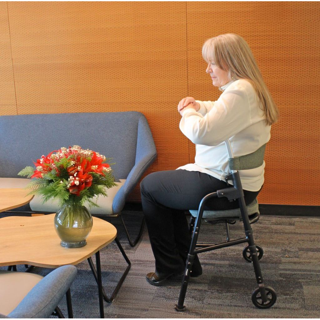 Person using a walker in a room with a gray couch and a table with flowers. - okotoks hc pharmacy