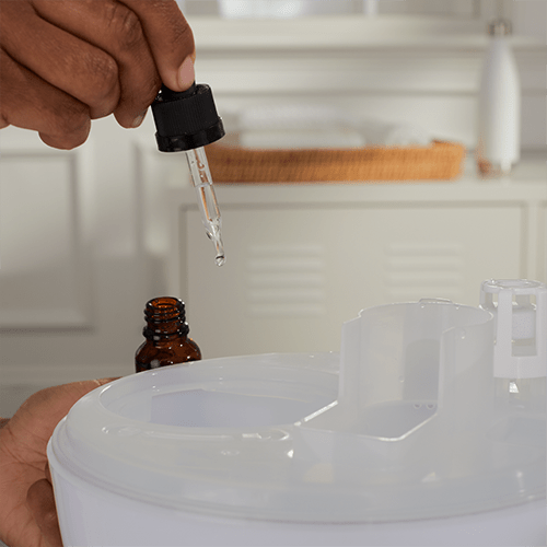 Hand using a dropper to add liquid from an amber bottle into a white container. - okotoks hc pharmacy