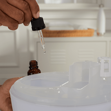 Hand using a dropper to add liquid from an amber bottle into a white container. - okotoks hc pharmacy